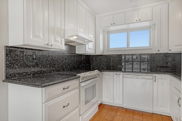 kitchen with light wood-type flooring, dark stone counters, white appliances, decorative backsplash, and white cabinets