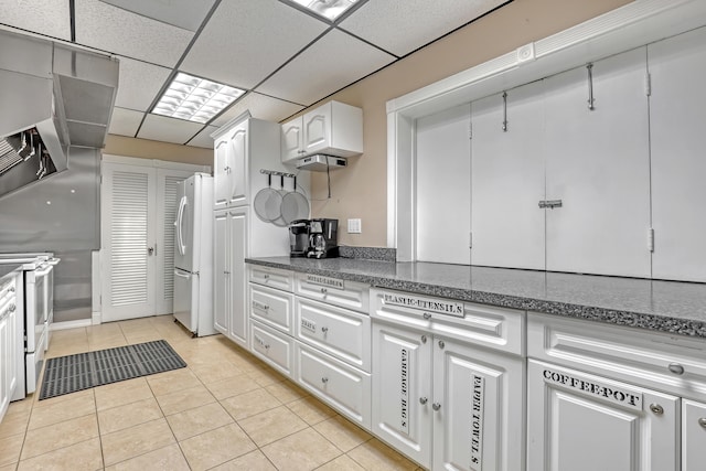 kitchen featuring refrigerator, light tile patterned floors, a paneled ceiling, white electric stove, and white cabinets