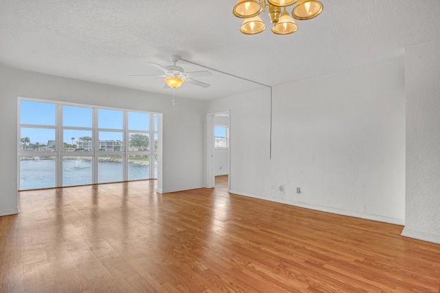 empty room featuring a textured ceiling, ceiling fan with notable chandelier, light wood-type flooring, and a water view