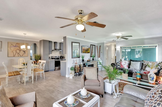 living room featuring a ceiling fan, crown molding, light wood-style floors, baseboards, and a textured ceiling