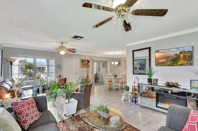 living room with ornamental molding, a textured ceiling, ceiling fan, and light hardwood / wood-style floors