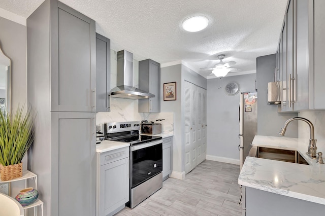 kitchen with stainless steel appliances, gray cabinets, wall chimney range hood, and ceiling fan