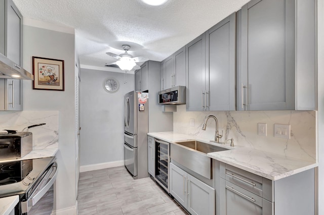 kitchen featuring a textured ceiling, stainless steel appliances, beverage cooler, light stone counters, and ceiling fan