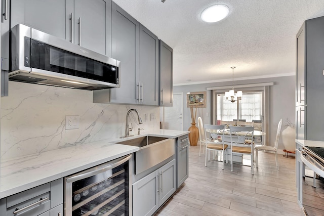 kitchen featuring beverage cooler, a notable chandelier, appliances with stainless steel finishes, ornamental molding, and sink