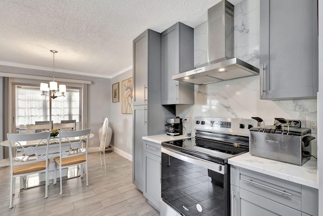 kitchen featuring stainless steel electric stove, a notable chandelier, hanging light fixtures, wall chimney range hood, and light wood-type flooring