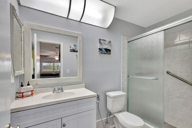 bathroom with tiled shower, toilet, vanity, and a ceiling fan