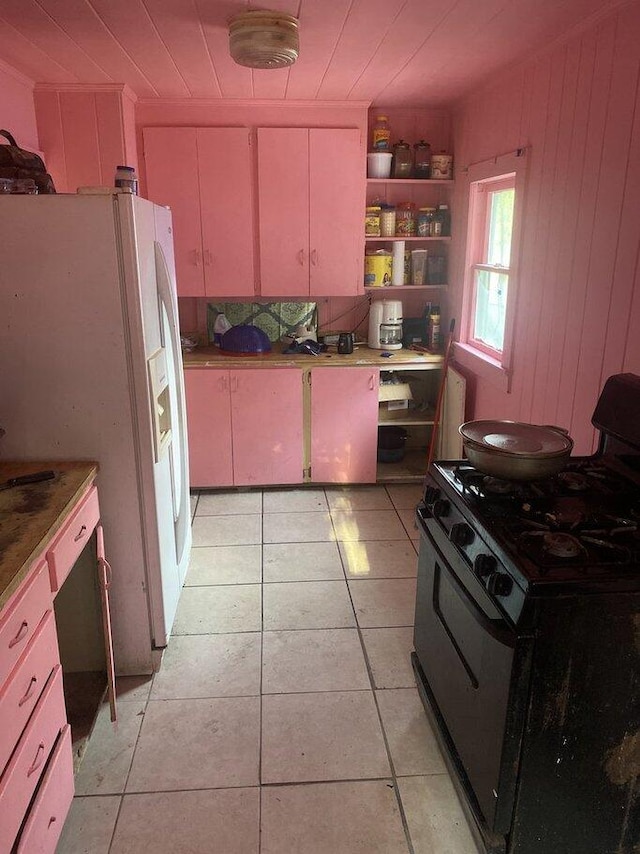 kitchen with wooden walls, black gas stove, light tile patterned flooring, and white fridge with ice dispenser