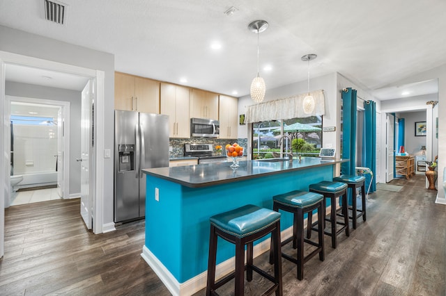 kitchen with light brown cabinetry, decorative light fixtures, appliances with stainless steel finishes, sink, and dark wood-type flooring