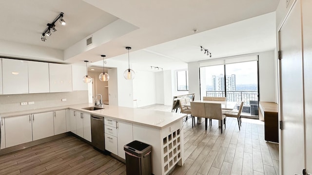 kitchen with sink, white cabinets, expansive windows, stainless steel dishwasher, and kitchen peninsula