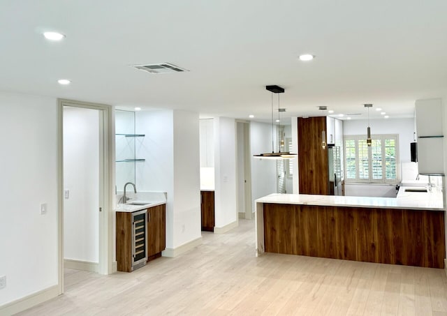 kitchen featuring pendant lighting, light hardwood / wood-style floors, and beverage cooler