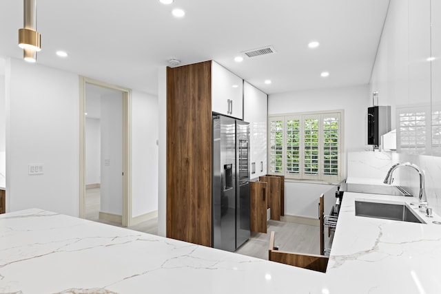 kitchen featuring light stone counters, pendant lighting, stainless steel refrigerator with ice dispenser, sink, and light hardwood / wood-style flooring