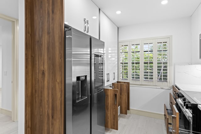 kitchen featuring white cabinetry, light wood-type flooring, stainless steel appliances, and light stone countertops