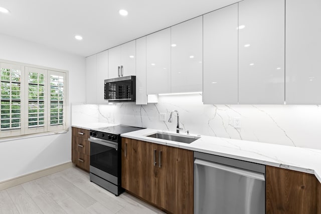 kitchen with stainless steel appliances, white cabinets, sink, light stone countertops, and light hardwood / wood-style flooring