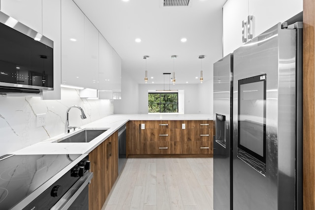 kitchen featuring stainless steel appliances, white cabinetry, decorative light fixtures, sink, and light hardwood / wood-style floors