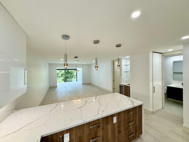 kitchen with hanging light fixtures, light stone countertops, wine cooler, and light wood-type flooring