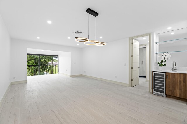 unfurnished living room with beverage cooler, indoor wet bar, and light wood-type flooring