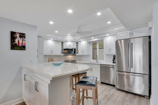 kitchen featuring white cabinets, a raised ceiling, stainless steel appliances, a kitchen bar, and sink