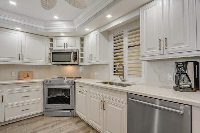 kitchen with ornamental molding, sink, white cabinetry, a tray ceiling, and stainless steel appliances