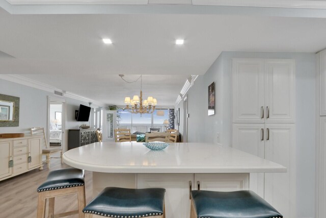 kitchen with light hardwood / wood-style floors, a breakfast bar area, an inviting chandelier, decorative light fixtures, and ornamental molding