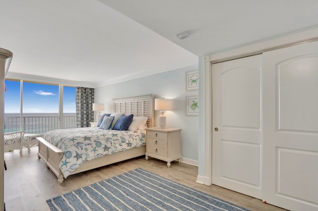 bedroom with ornamental molding, a closet, a wall of windows, and hardwood / wood-style flooring