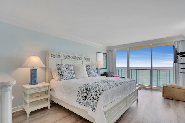 bedroom with wood-type flooring, access to exterior, a water view, ornamental molding, and a wall of windows