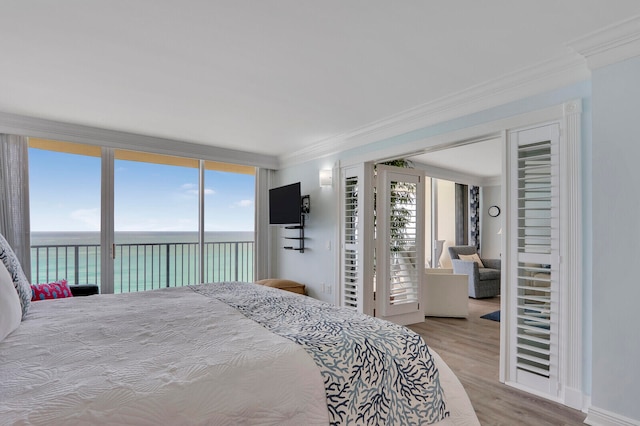 bedroom with light wood-type flooring, a water view, ornamental molding, and access to exterior