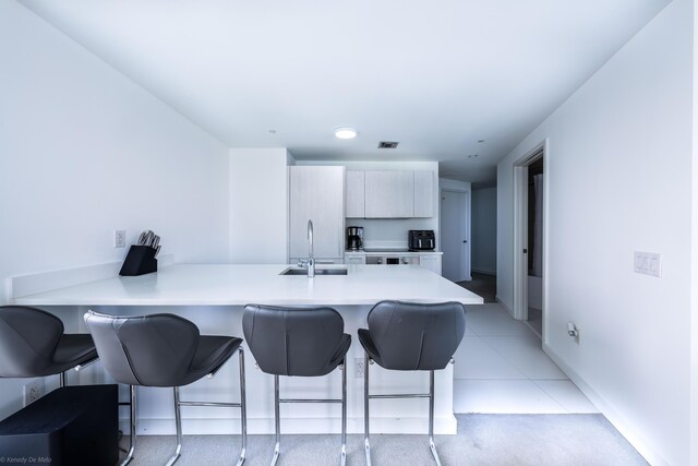 kitchen with light tile patterned floors, a breakfast bar, kitchen peninsula, and sink