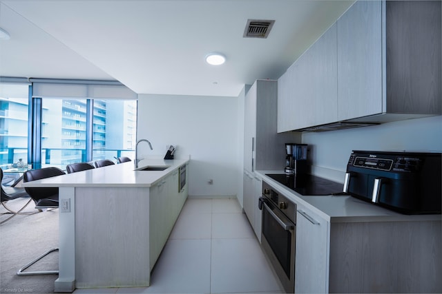 kitchen with light tile patterned floors, oven, sink, black electric cooktop, and a kitchen breakfast bar