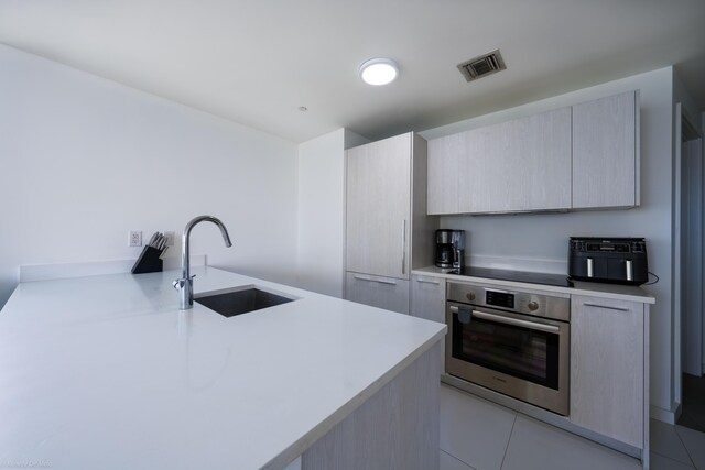 kitchen with light tile patterned floors, light brown cabinets, stainless steel oven, and sink