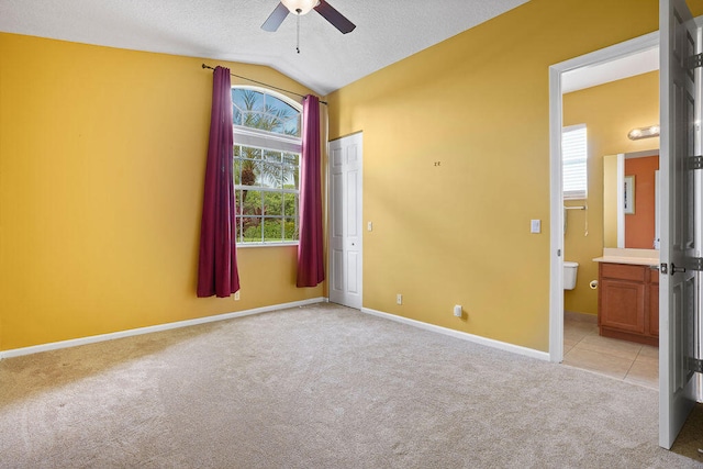 unfurnished bedroom featuring ensuite bath, vaulted ceiling, light colored carpet, ceiling fan, and a textured ceiling