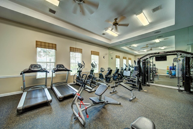 workout area featuring a tray ceiling, ceiling fan, and a textured ceiling