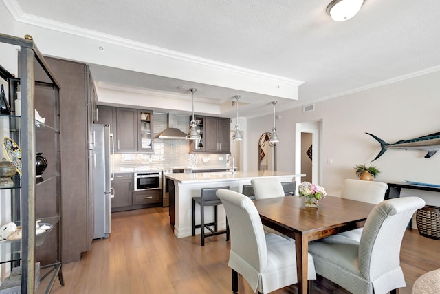 dining room featuring sink, crown molding, a textured ceiling, and light wood-type flooring