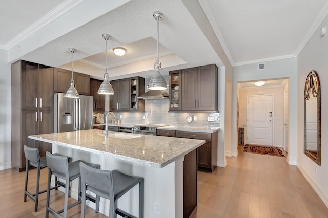 kitchen with appliances with stainless steel finishes, a textured ceiling, a kitchen island with sink, light hardwood / wood-style flooring, and light stone counters