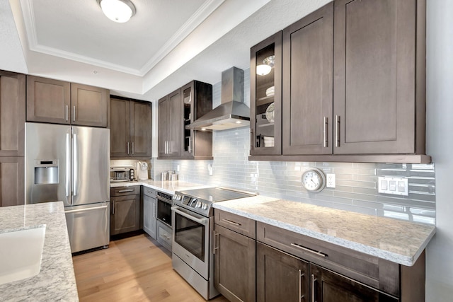 kitchen featuring light stone counters, light hardwood / wood-style flooring, crown molding, wall chimney exhaust hood, and stainless steel appliances