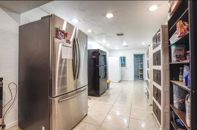 kitchen with a textured ceiling, black fridge, white fridge, stainless steel refrigerator, and light tile patterned floors