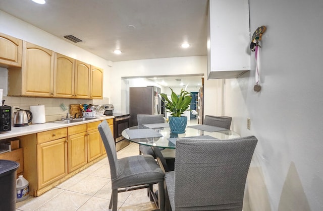 kitchen featuring sink, backsplash, appliances with stainless steel finishes, light tile patterned floors, and light brown cabinetry