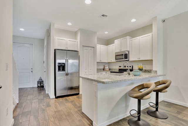 kitchen with sink, white cabinetry, light stone countertops, light hardwood / wood-style floors, and stainless steel appliances