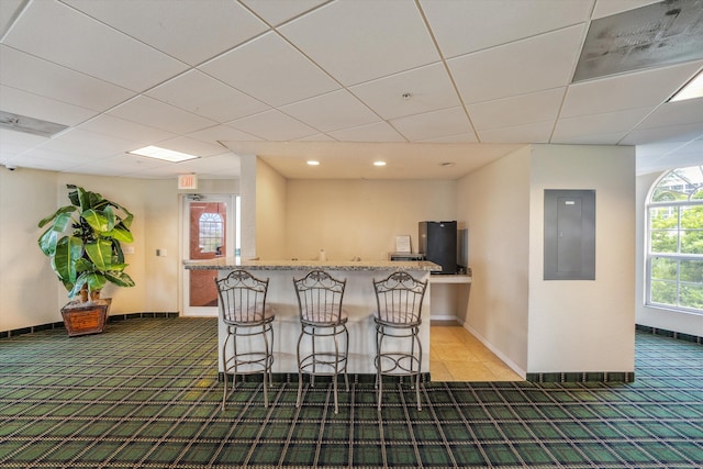 kitchen featuring a center island, electric panel, carpet floors, a breakfast bar area, and a paneled ceiling