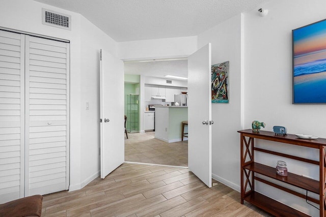 hallway with a textured ceiling and light hardwood / wood-style flooring