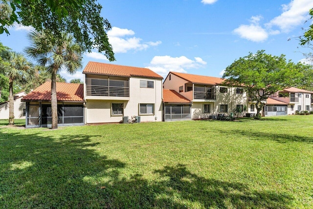 rear view of house with central air condition unit, a lawn, and a sunroom