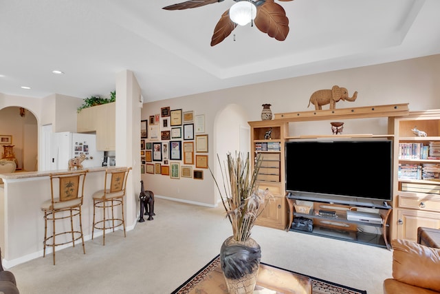 carpeted living room with ceiling fan and a raised ceiling