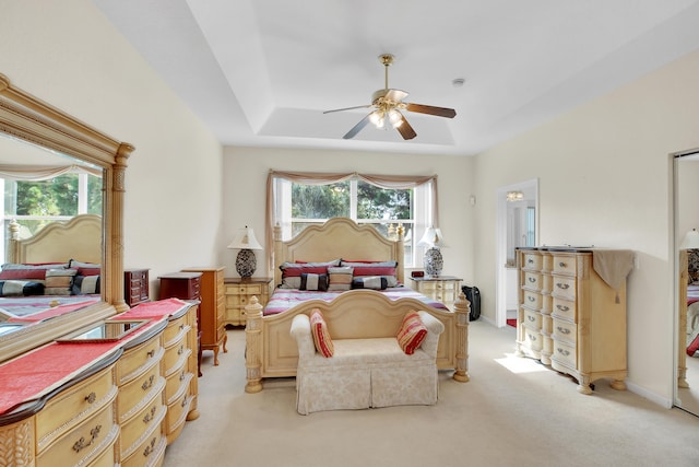 bedroom with multiple windows, ceiling fan, a raised ceiling, and light carpet