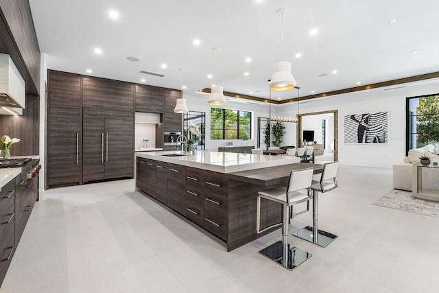 kitchen with dark brown cabinetry, sink, a large island with sink, decorative light fixtures, and a breakfast bar area