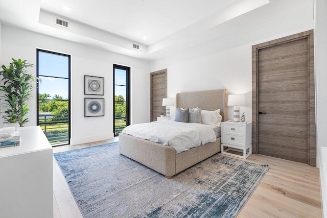 bedroom featuring access to exterior, light hardwood / wood-style floors, and a tray ceiling