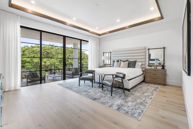 bedroom featuring access to exterior, a raised ceiling, and light hardwood / wood-style flooring