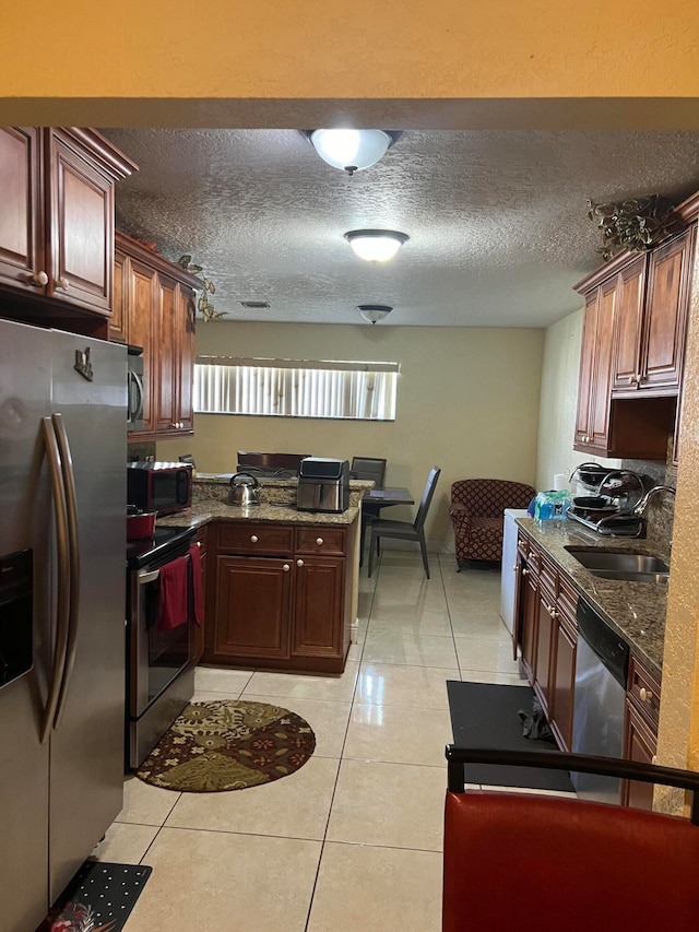 kitchen with dark stone countertops, a textured ceiling, stainless steel appliances, and light tile patterned flooring