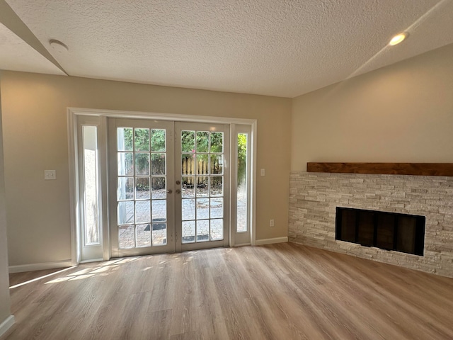 unfurnished living room with a textured ceiling, light wood-type flooring, french doors, and a fireplace