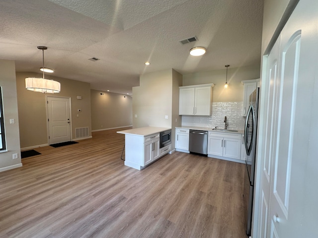 kitchen with white cabinets, appliances with stainless steel finishes, light hardwood / wood-style floors, kitchen peninsula, and pendant lighting