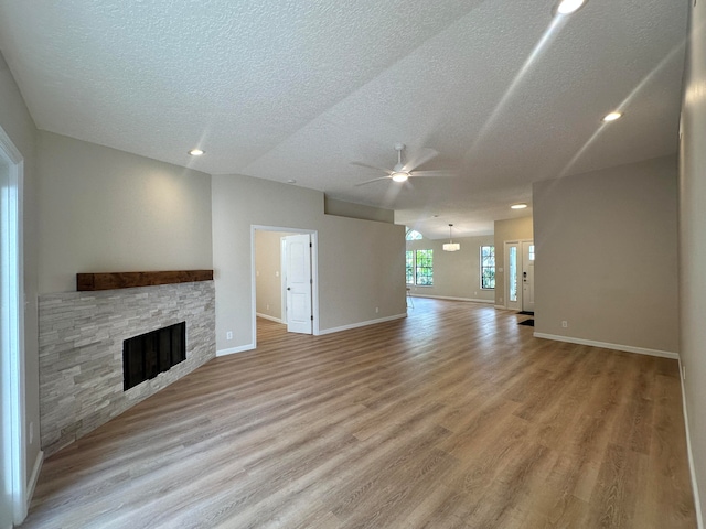 unfurnished living room with light wood-type flooring, ceiling fan, a fireplace, and a textured ceiling