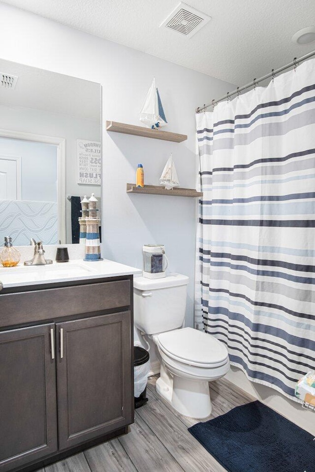 bathroom with wood-type flooring, a textured ceiling, vanity, and toilet